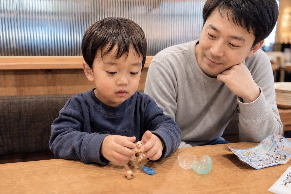 飲食店でガチャのおまけで喜んで遊ぶ子供と親